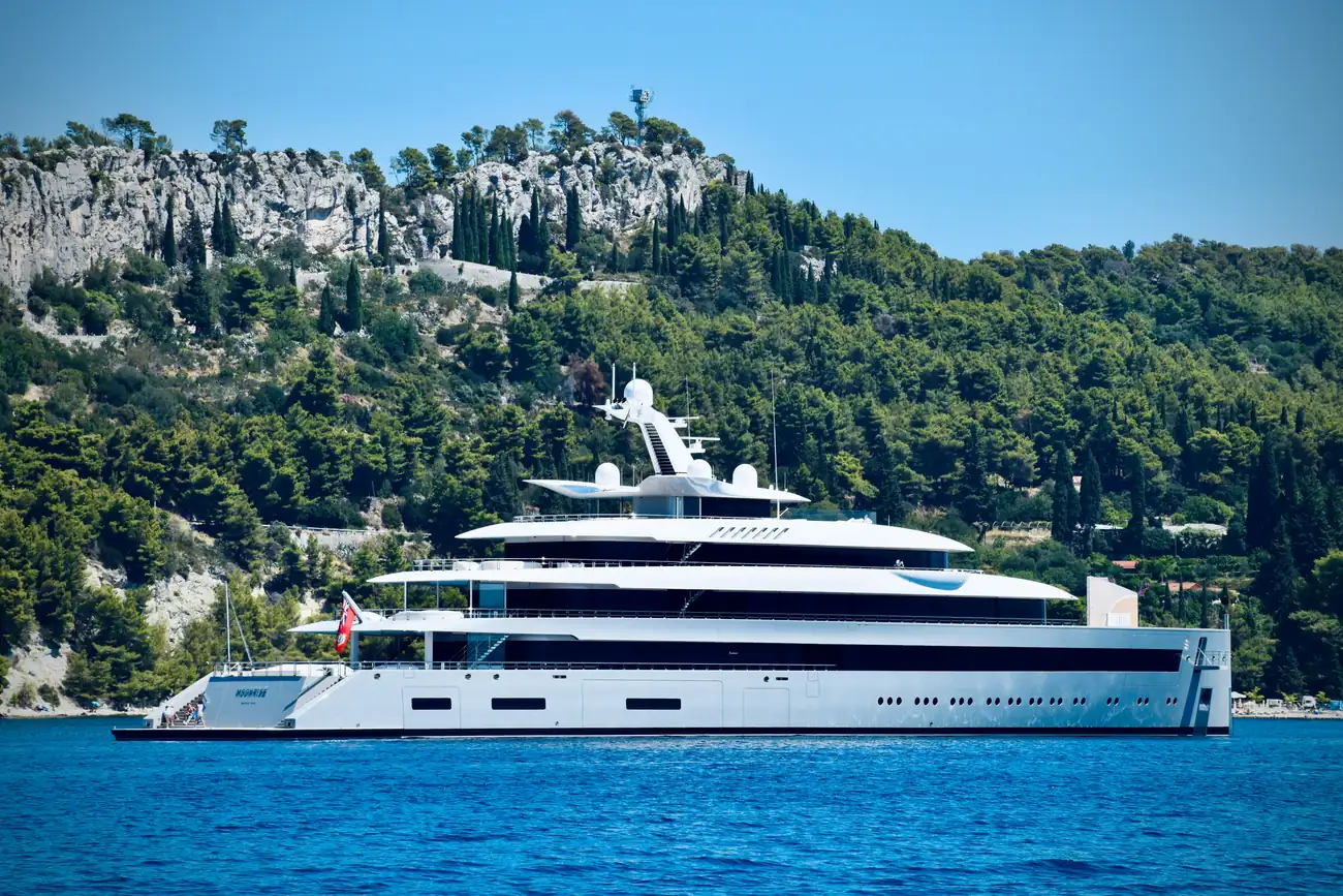 Large yacht moving along a rocky green coastline