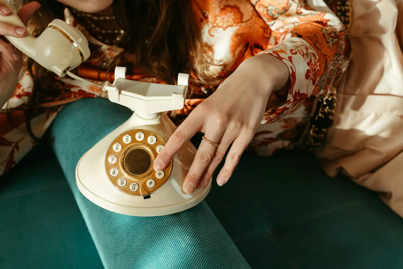 A hand dialing a cream rotary phone on a green chair