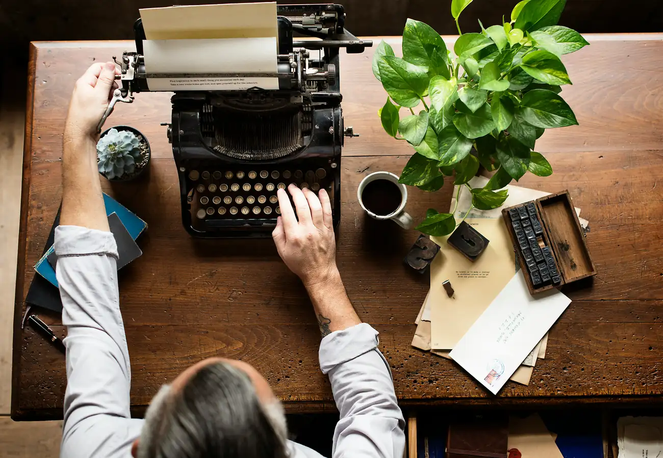 Hands working at a vintage typewriter on a wooden desk